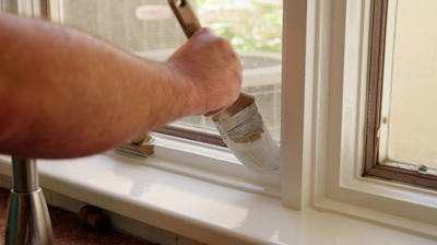 Painter uses high gloss paint finish white paint to repaint a windowsill