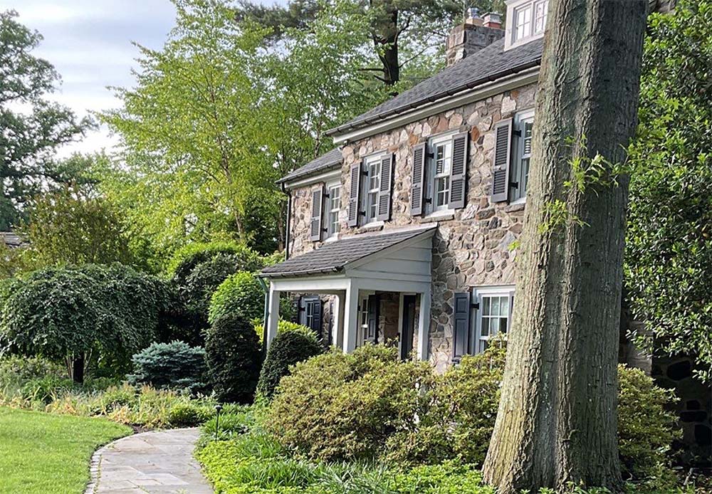 Stone home exterior painting project in Haverford PA with black shutters and professionally painted trim by Groovy Hues Painting of Philadelphia