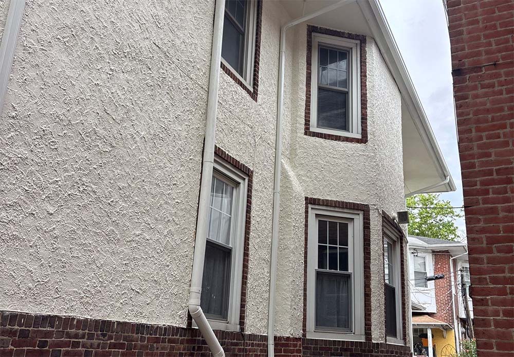 Stucco exterior painting project in Philadelphia PA featuring freshly painted white stucco walls and brick trim by Groovy Hues Painting of Philadelphia