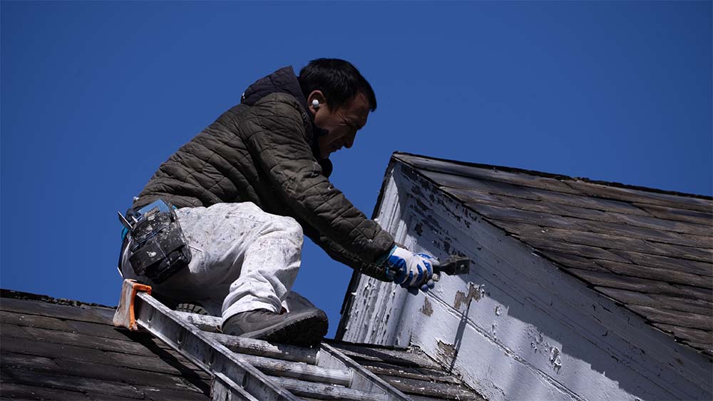 Professional painter preparing exterior trim and siding before painting on a Bucks County home