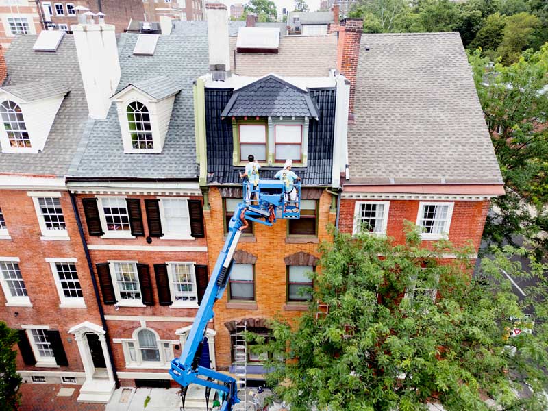 Professional exterior painters using an aerial lift to paint a multi-story historic building in Philadelphia